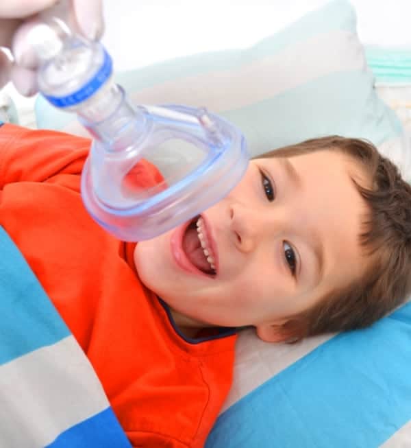 A young child smiling with an oxygen mask placed a few inches from his mount and nose.