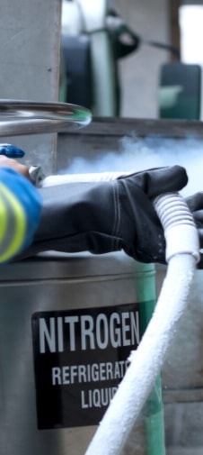 A person wearing thick black gloves holding a frozen cable connected to a nitrogen tank.