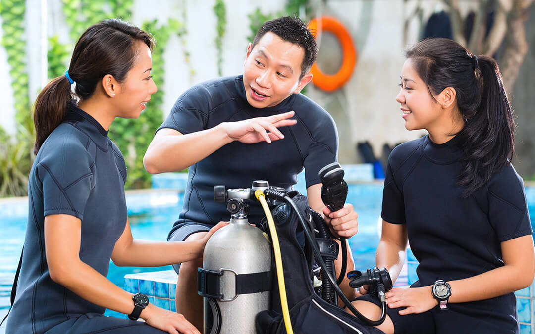Three scuba divers talking. In the center is an oxygen tank.
