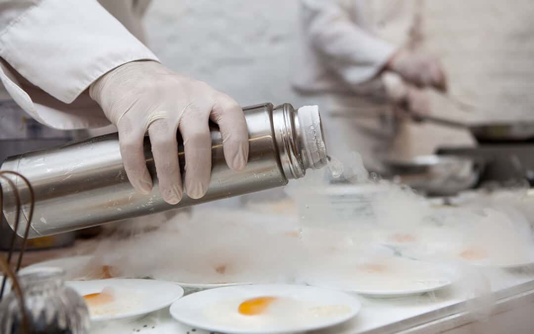 A chef pouring liquid nitrogen onto a row of plated eggs.