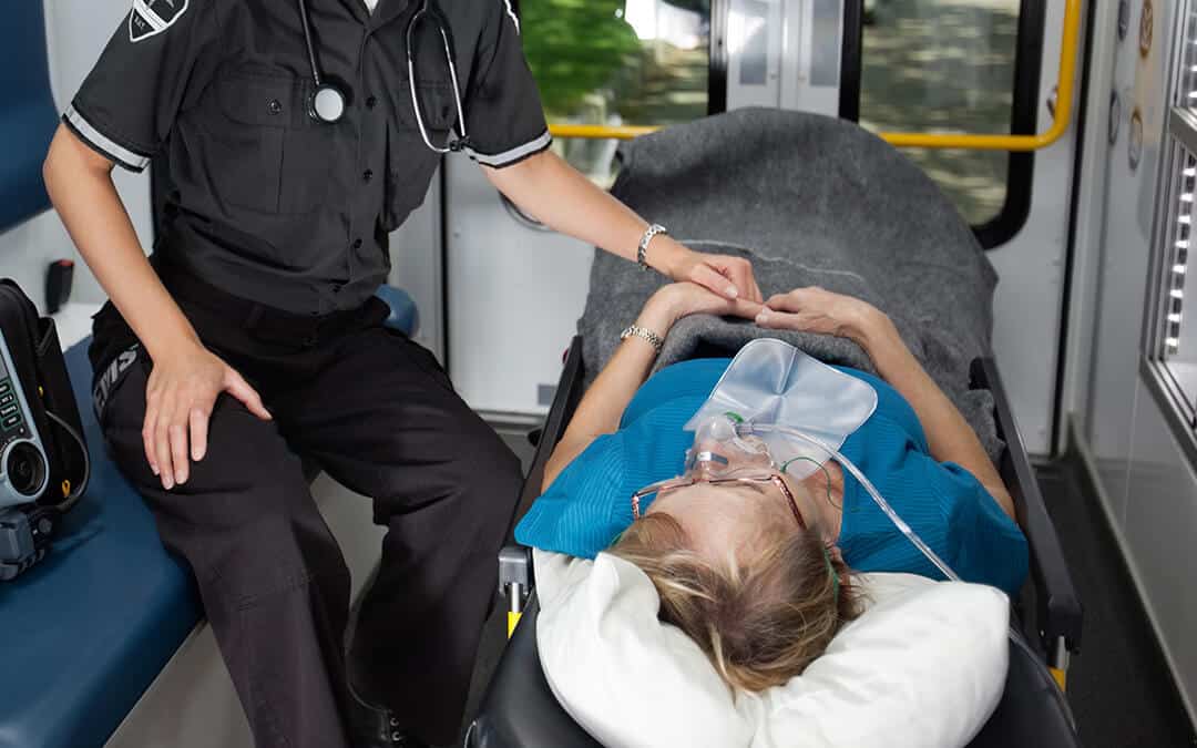 Woman laying on a stretcher in an Ambulance being taken care of by an EMT.