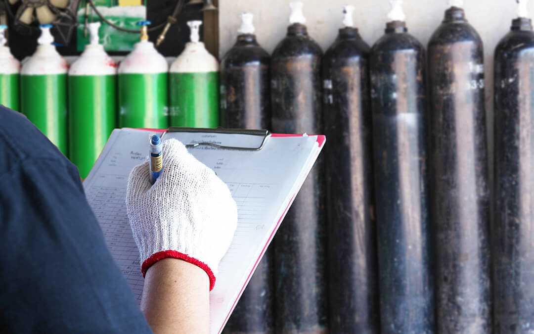 Technitian writing on a clipboard with a row of oxygen tanks in the background.