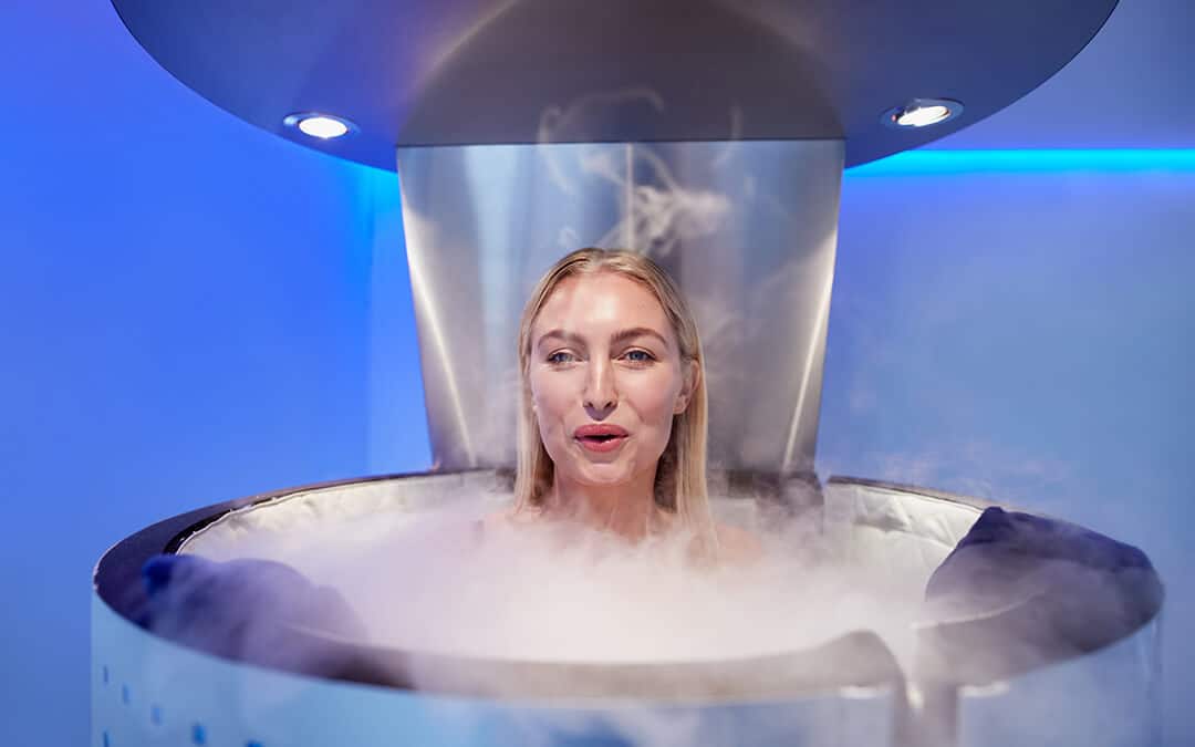 Happy young woman in a whole body cryotherapy cabin. She is looking at camera and smiling.