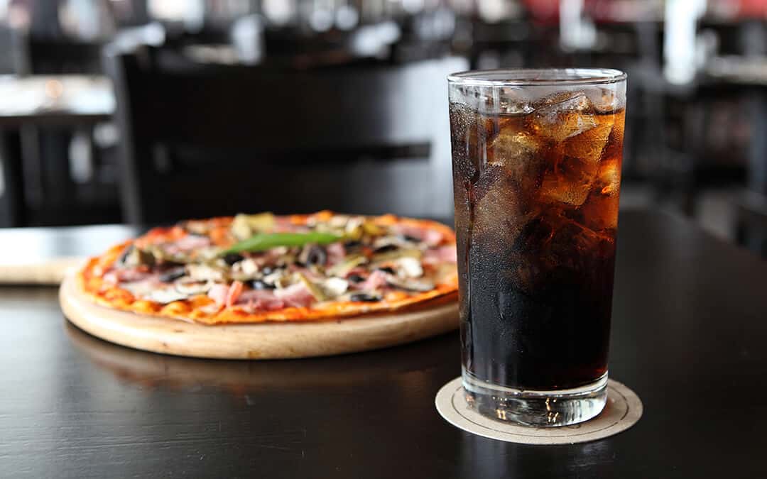 Glass with coca cola and pizza on background
