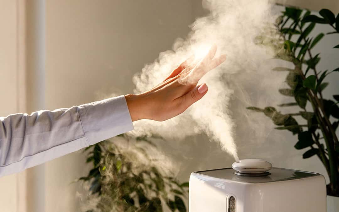 Woman holds hand over steam from an air humidifier. 