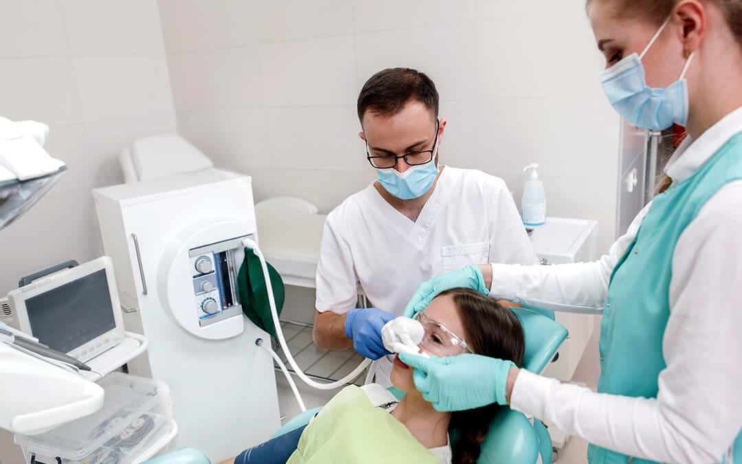 Dentist and his assistant using inhalation sedation on young girl before dental treatment
