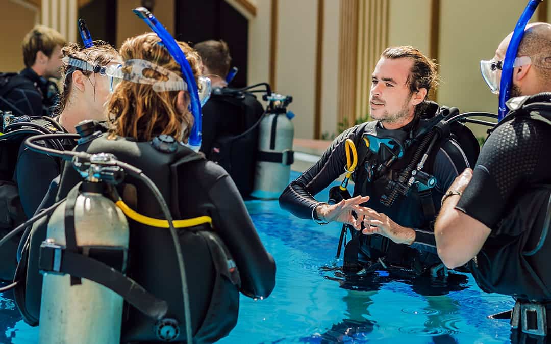 Scuba diving students in a swimming pool with scuba tanks on their backs