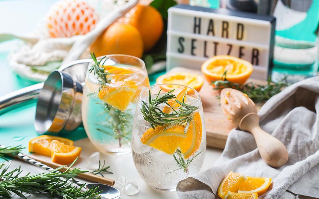 Two glasses with clear hard seltzer with orange slices