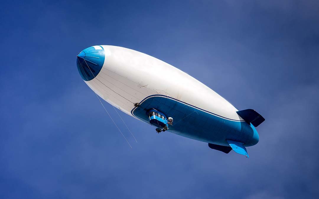 Blue and white blimp on a sunny day floating with a blue sky background.