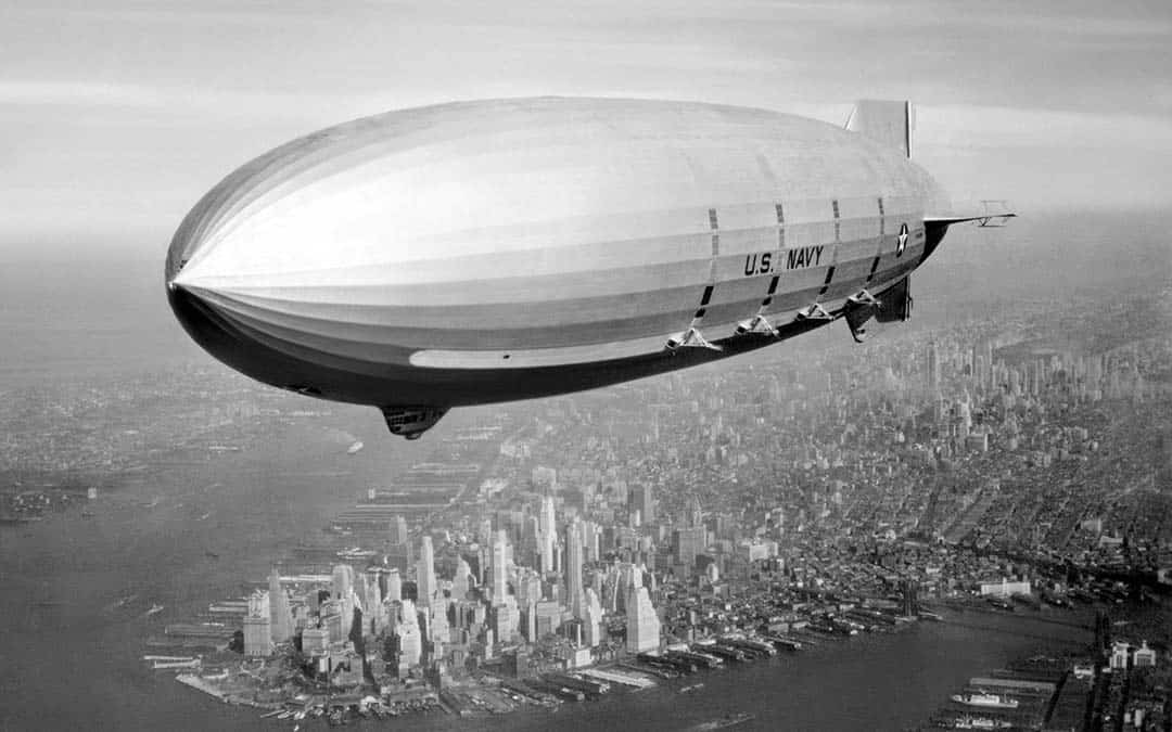 Historical black and white photo of a blimp flying over New York City