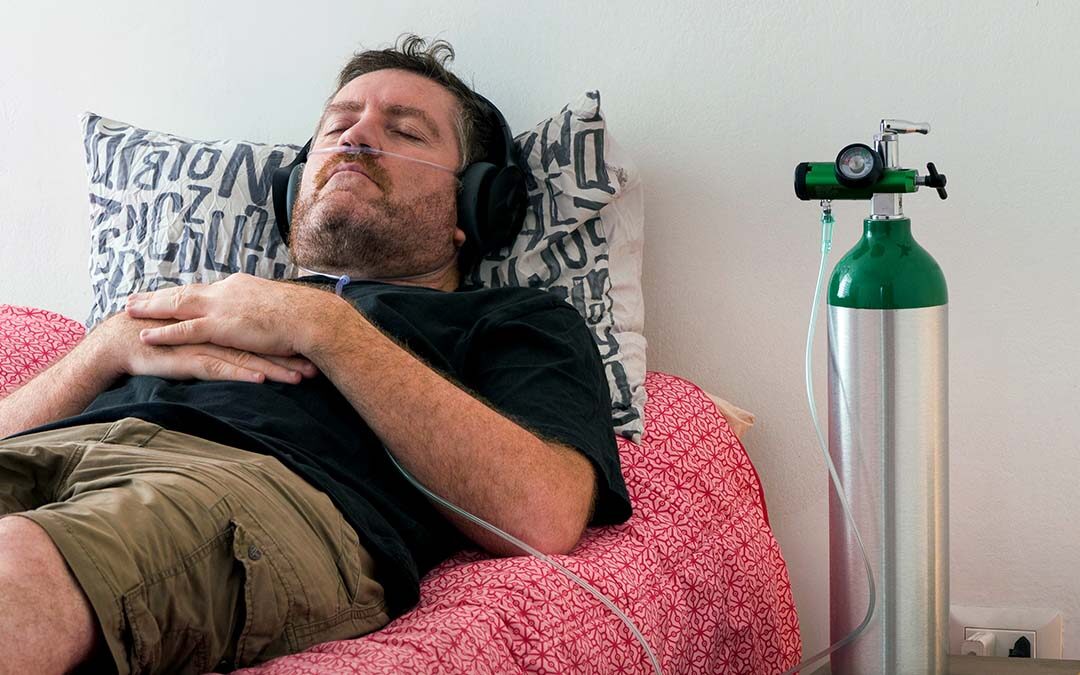 A man lying down on a bed breathing oxygen from a cylinder