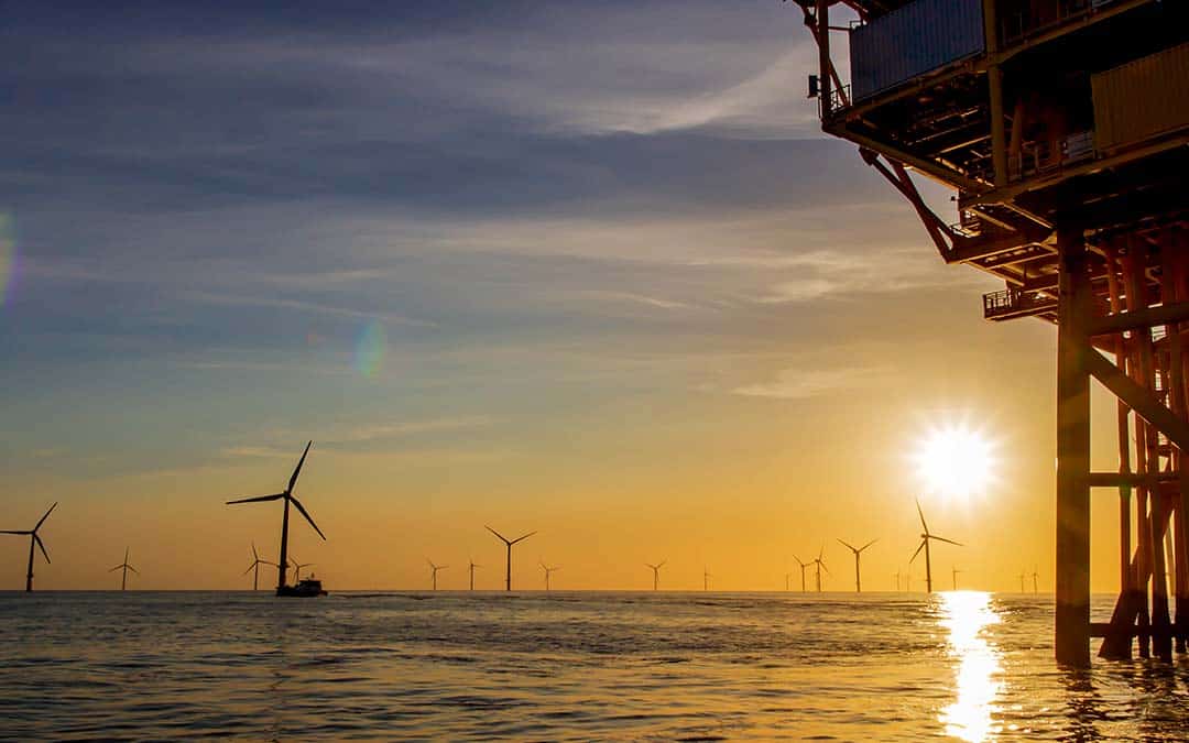 windmills in a body of water with sunset in the background